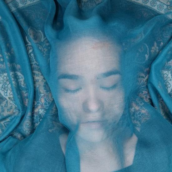 Billedet forestiller en kvinde liggende under et gennemsigtig sjal i en blålig farve.