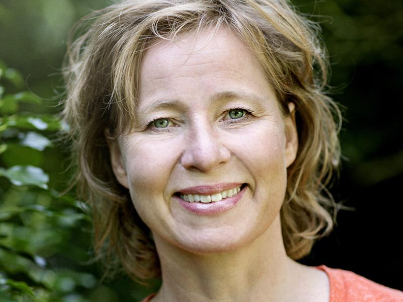 Billedet viser en smilende Anette Sams foran en grøn busk