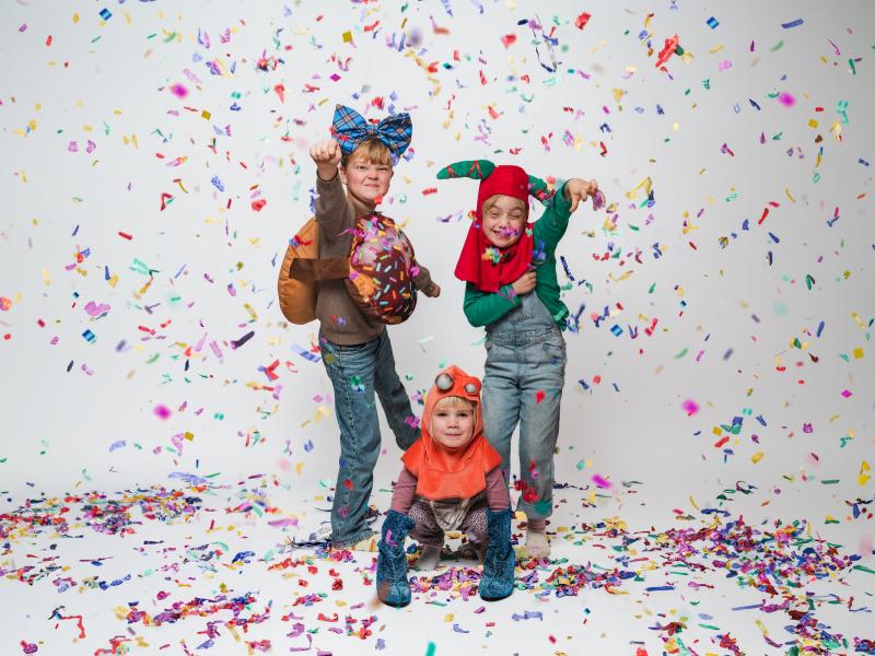 Billedet viser tre børn i en mængde farvestrålende konfetti