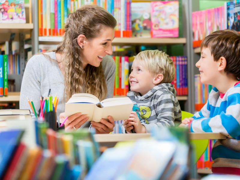 Billedet viser en smilende kvinde, der læser højt for to børn