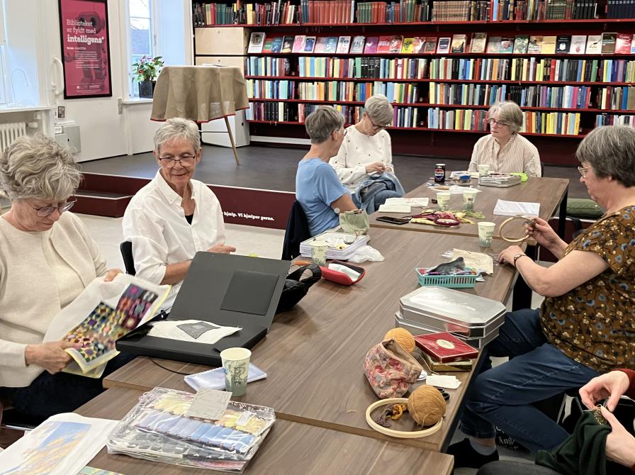 Billedet viser en gruppe kvinder, som sidder rundt om et bord og broderer