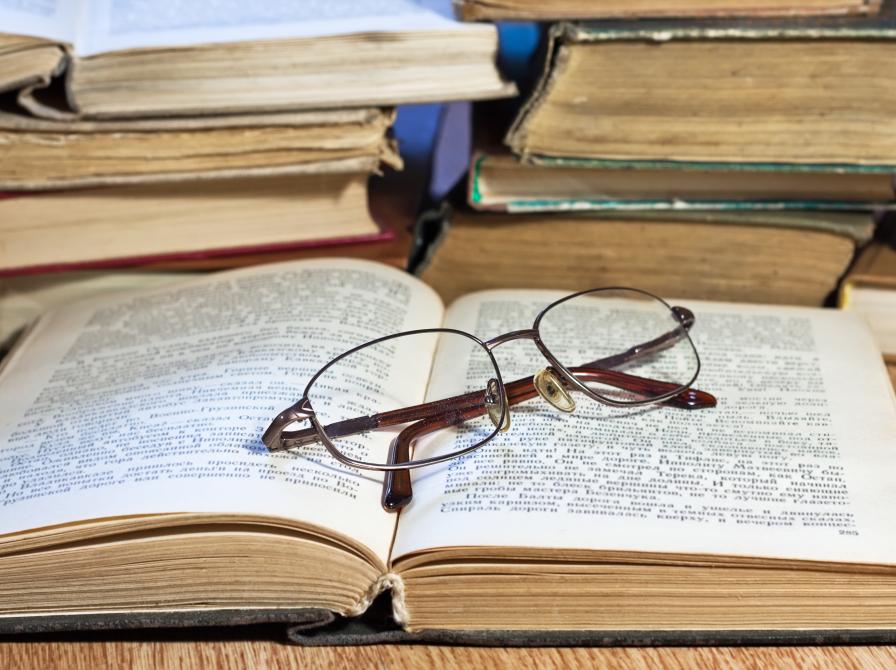 Billedet viser en opslået bog med et par briller ovenpå